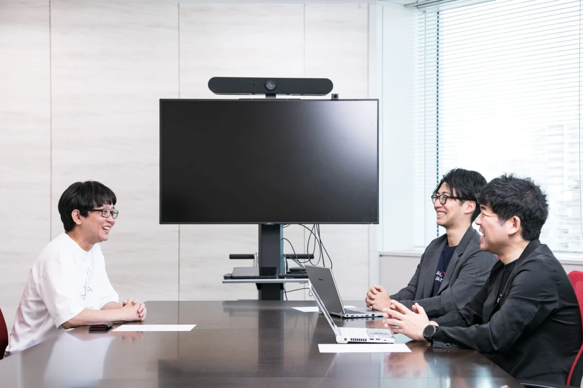 会議室のモニターを前に談笑する、株式会社リバネスナレッジ 古泉 賢人（左）と、フジテック株式会社 小畑 俊介 氏・佐竹 右教 氏（右）