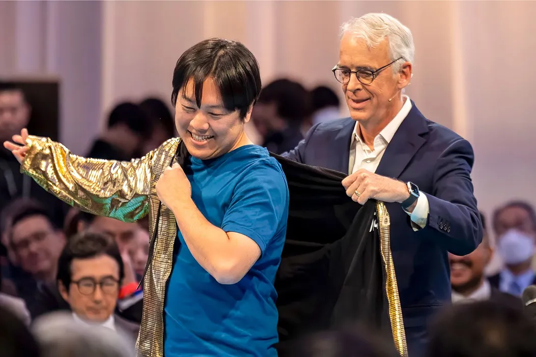 Agentforce World Tour Tokyo 2025の会場で、Salesforce共同創業者兼 Slack最高技術責任者のParker Harris氏(右)から金色のGolden Hoodieを着せられ、笑顔を見せる株式会社リバネスナレッジ代表取締役社長の吉田丈治(左)