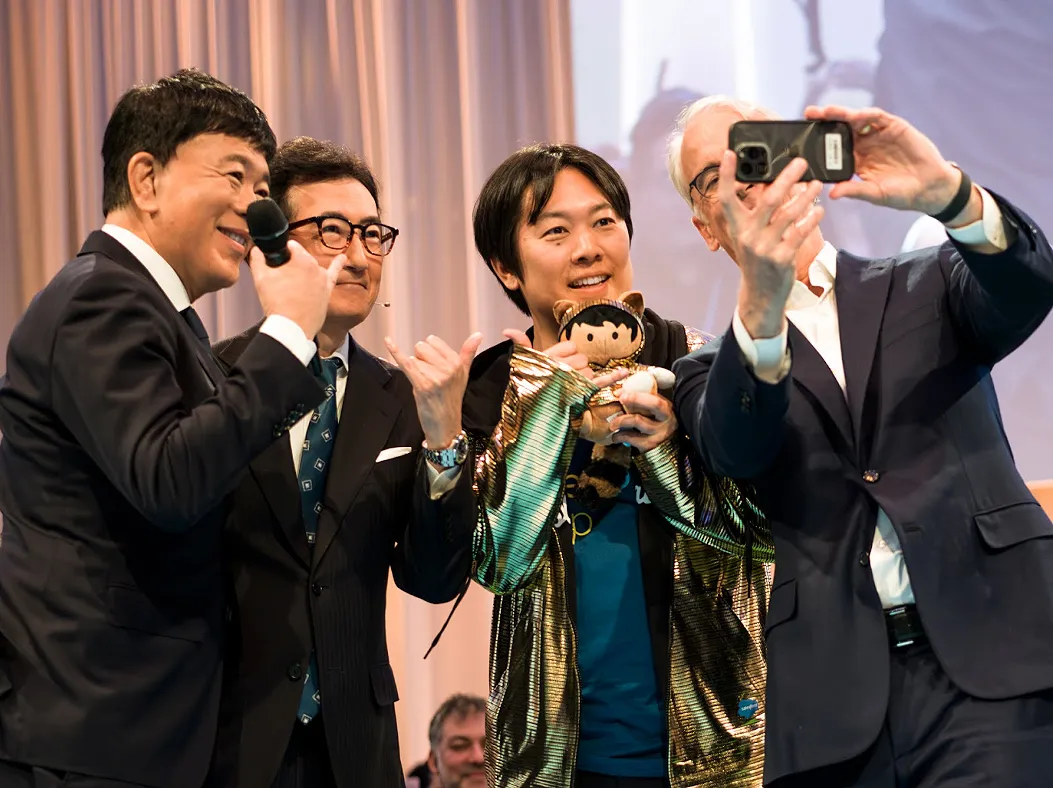 Golden Hoodieを着てSalesforceのマスコット人形を抱えた吉田丈治(中央)と、スマートフォンを掲げて記念撮影するParker Harris氏(右)、登壇者2名(左)がAgentforce World Tour Tokyo 2025の壇上に並ぶ様子